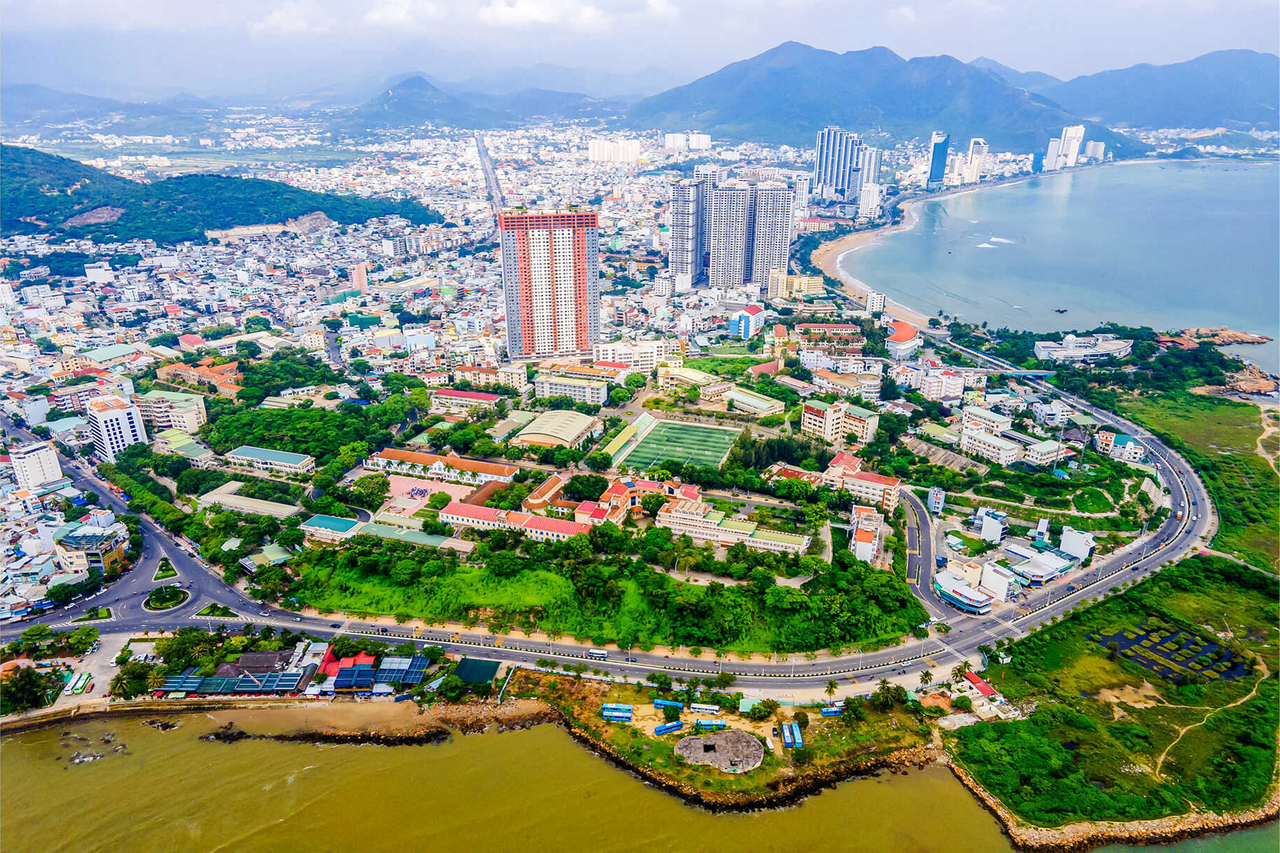 Aerial view of Nha Trang College of Technology in Vietnam, showing the campus surrounded by urban buildings, coastal shoreline, and mountainous landscape.