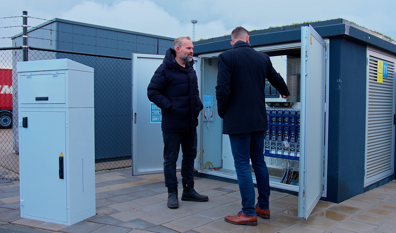 Two technicians inspecting an open outdoor electrical control cabinet